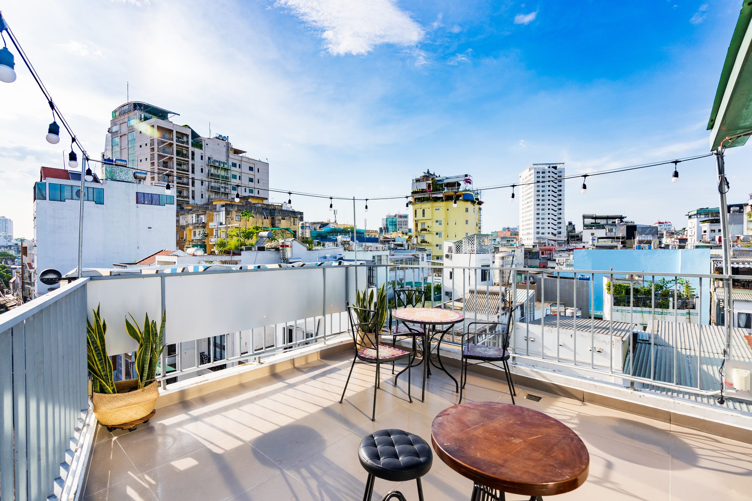 Rooftop terrace at an Ekomo Home property, strung with lights at dusk over the Saigon skyline